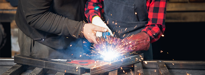 Two people welding metal together in a Wisconsin workshop, bright sparks flying around them.