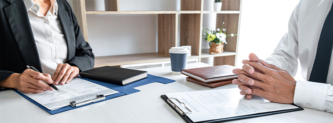 Two people in business attire discuss Wisconsin State Assembly documents over coffee at a desk.